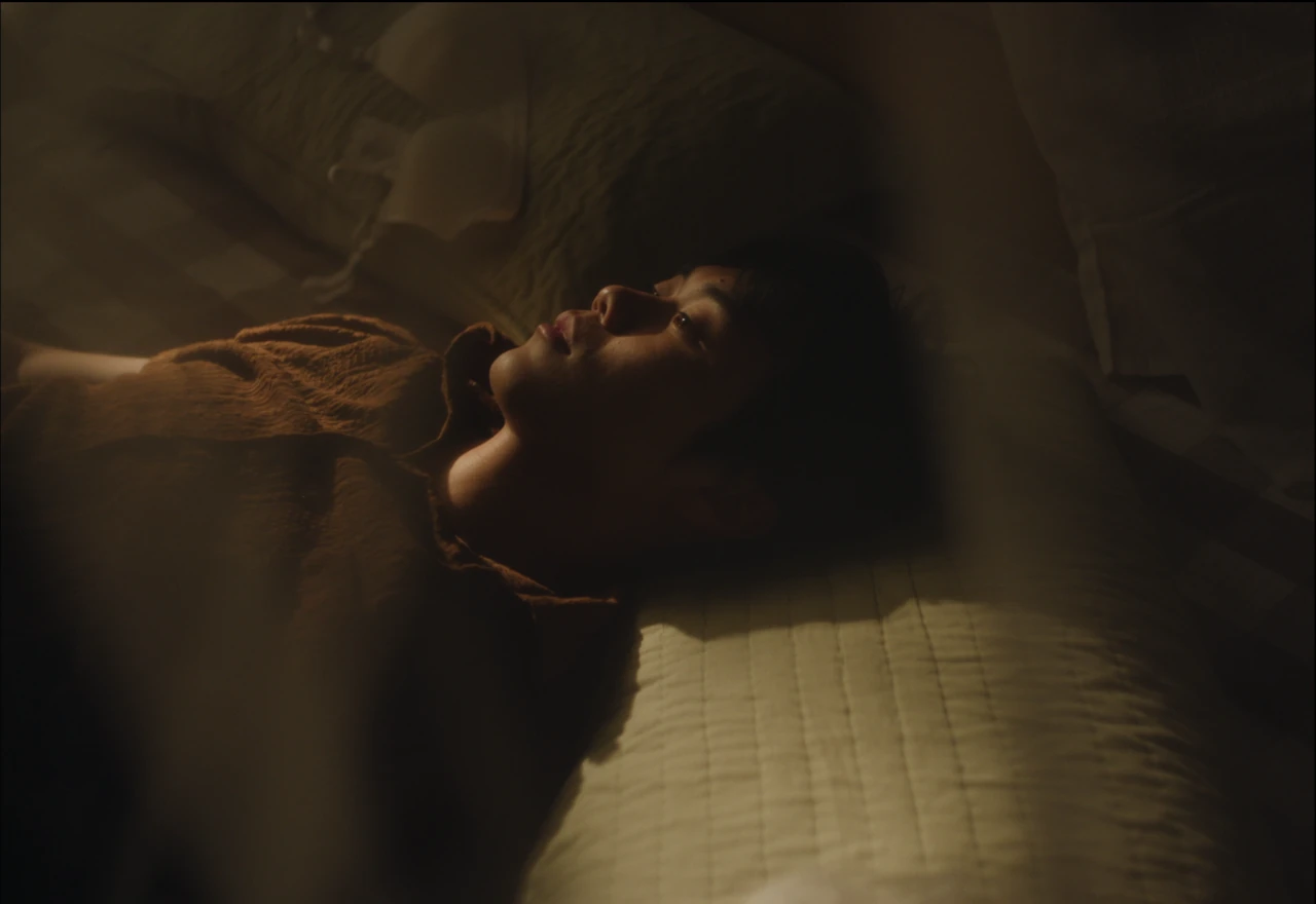 A young person lying on a bed in warm, dim light.
