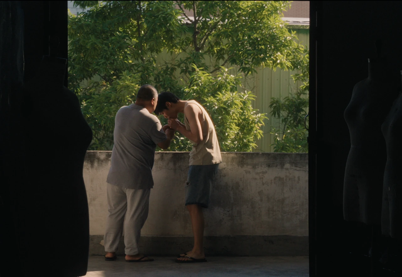 Two people leaning close together beside a courtyard wall beneath green branches.