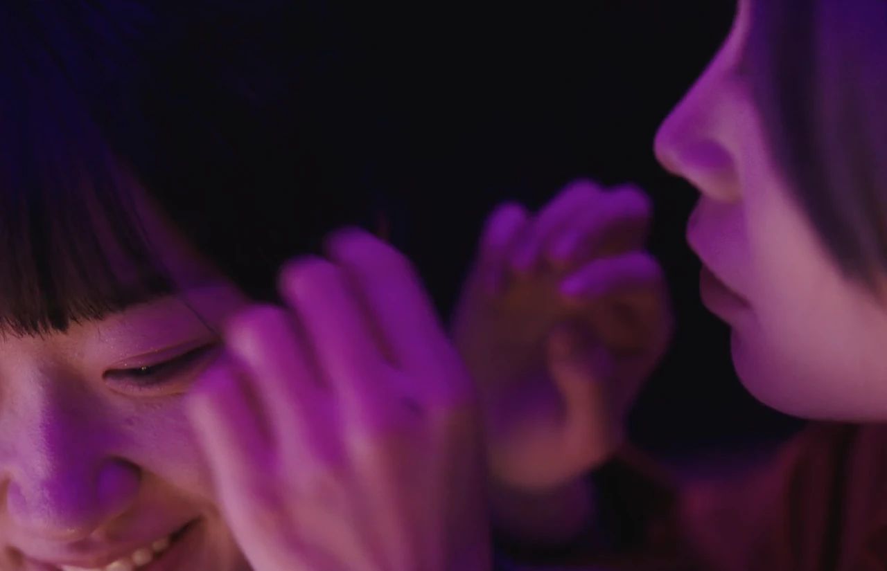 Two people face each other in a close-up under purple lighting.