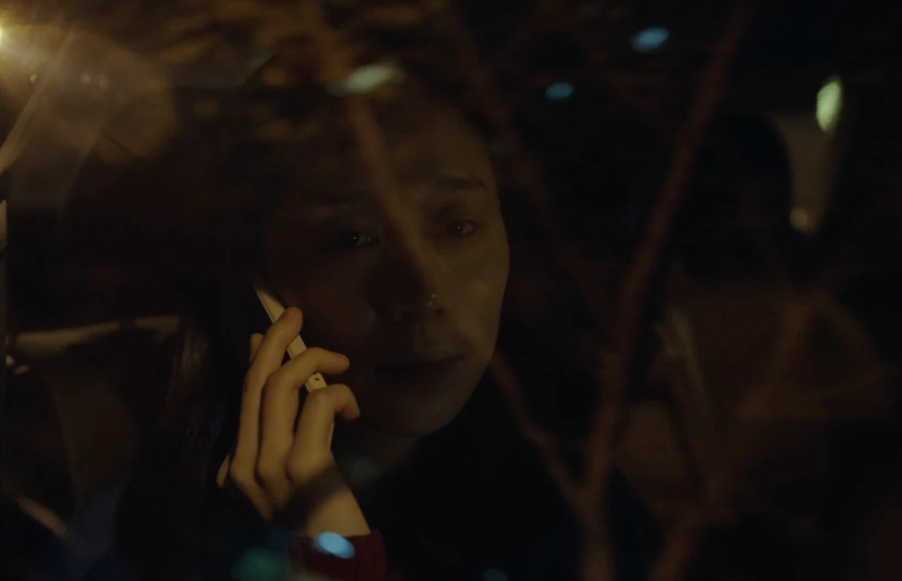 A man holds a phone to his ear, seen through a reflective window at night.