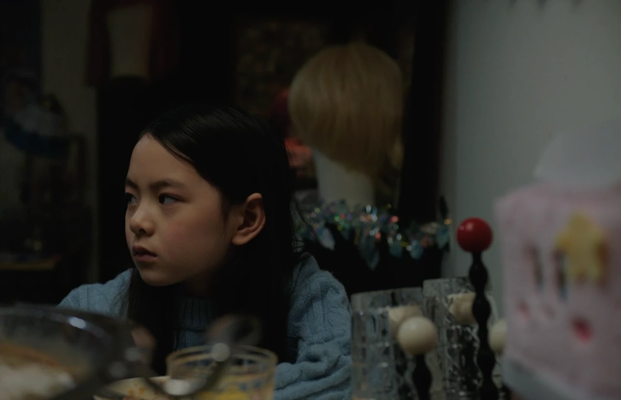 A young girl sits at a table with a wig displayed behind her.