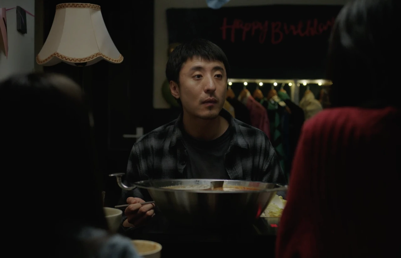 A man holding chopsticks sits at a birthday table opposite a woman in red.