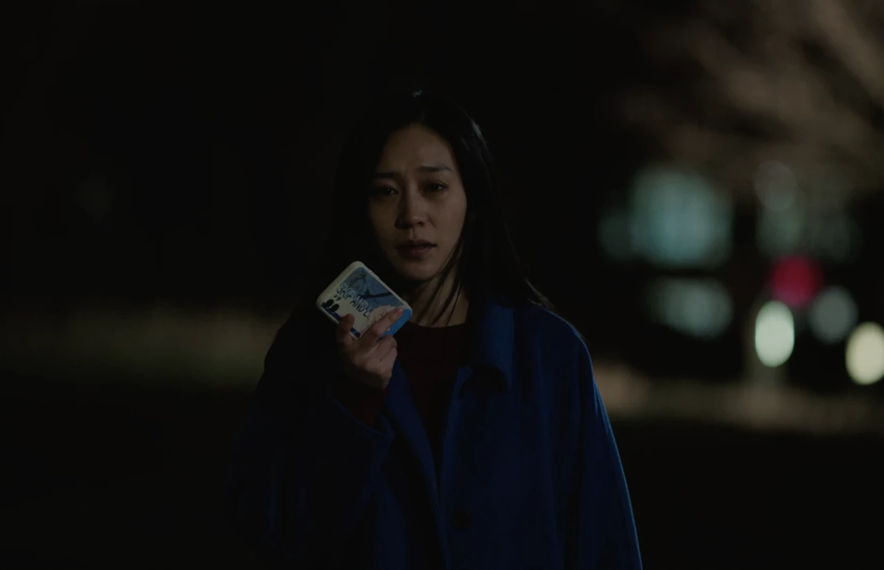 A woman in a blue coat holds up a small printed photograph at night.